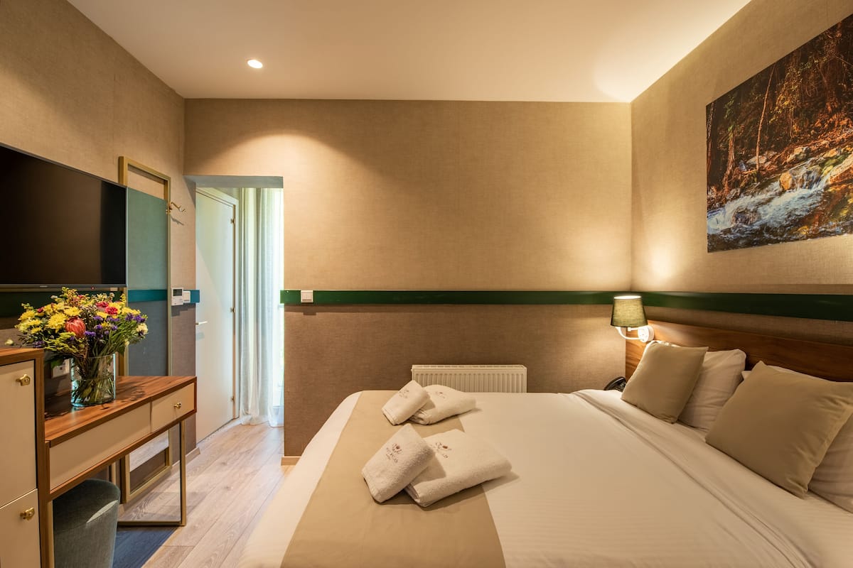 A hotel room with a bed, a desk, a TV, and a painting on the wall.
