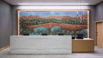 A reception desk with a mosaic wall behind it, a wooden door to the right, and a modern light fixture above.