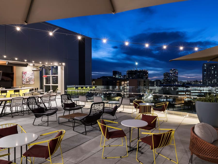 Um bar no terraço com mesas ao ar livre, vista da cidade e luzes de corda.