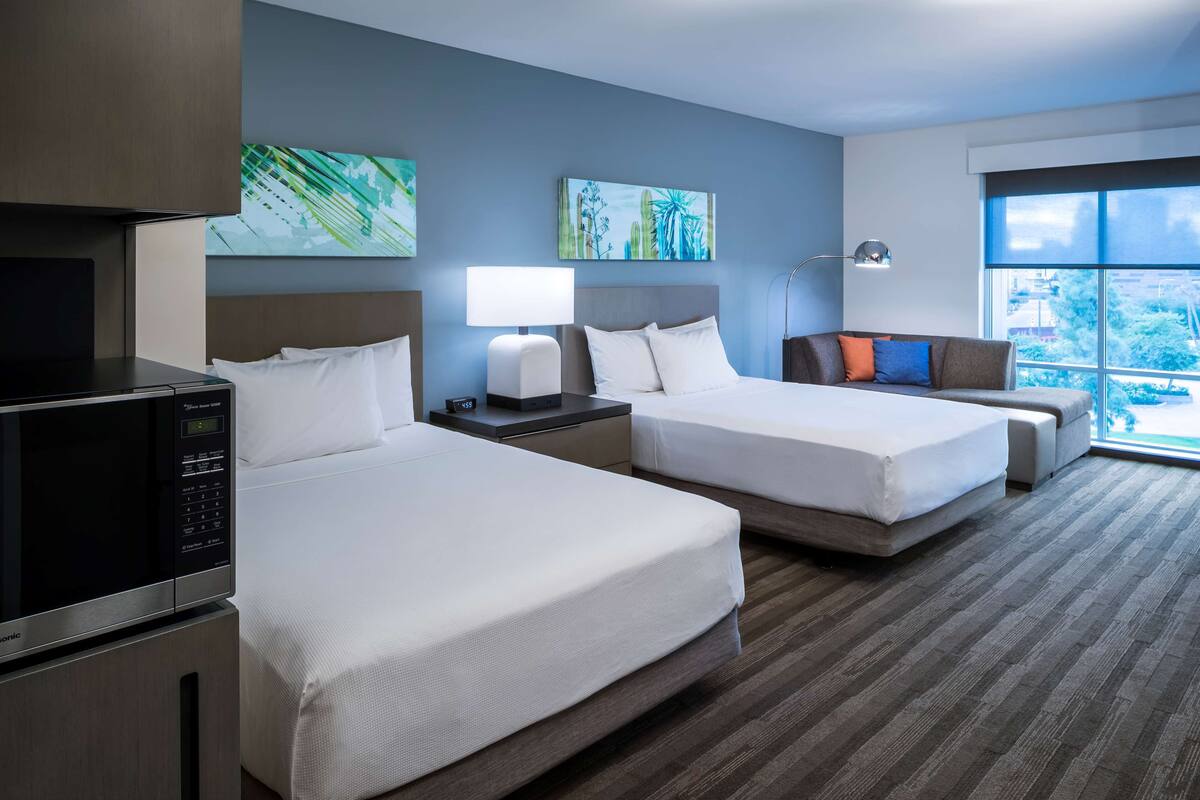 Habitación de hotel con dos camas, microondas, escritorio con lámpara y obras de arte en las paredes.