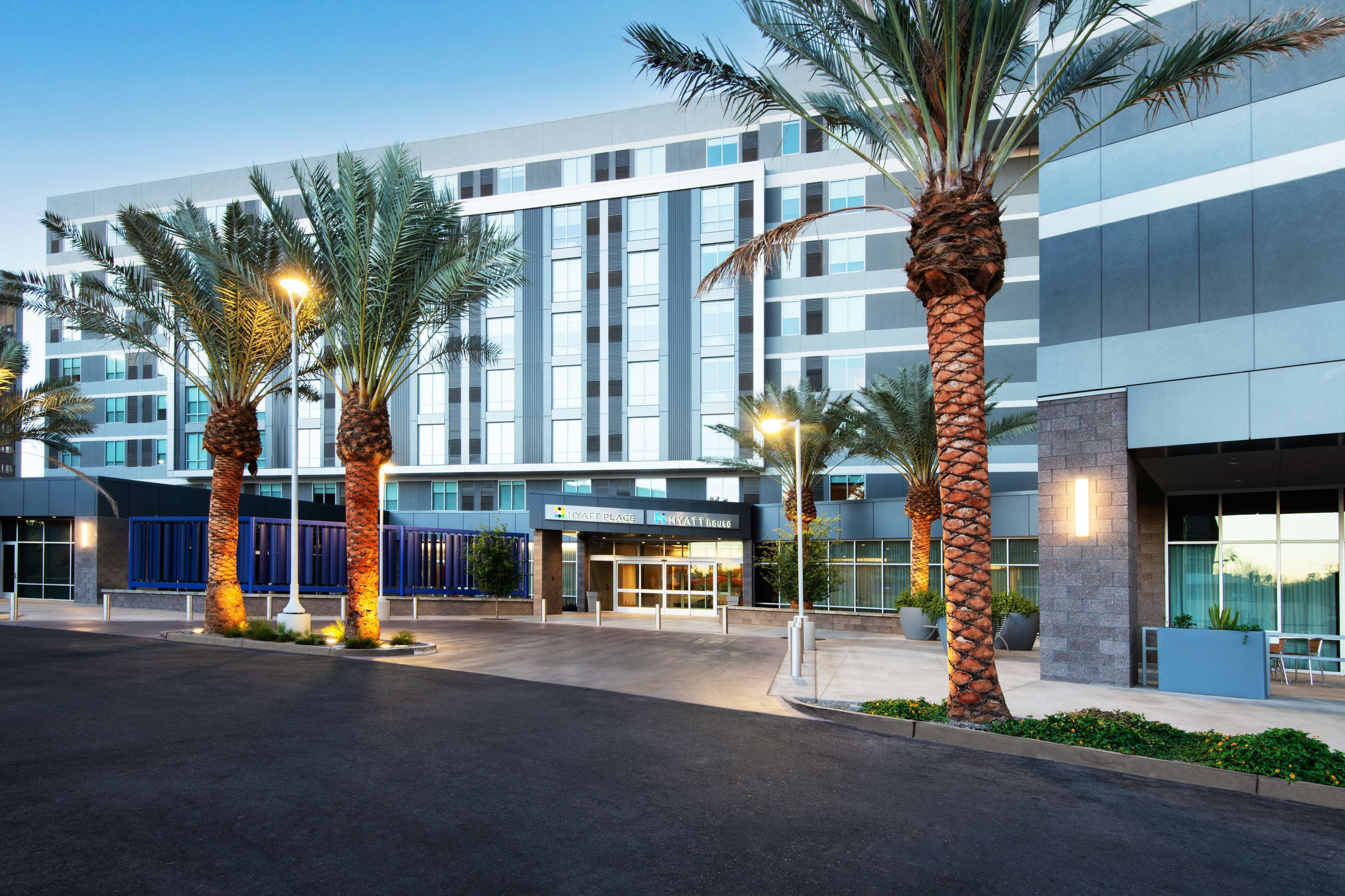 A modern hotel with a glass facade, palm trees, and a well-lit entrance.