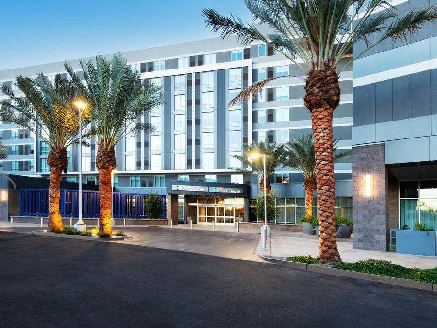 A modern hotel with a glass facade, palm trees, and a well-lit entrance.