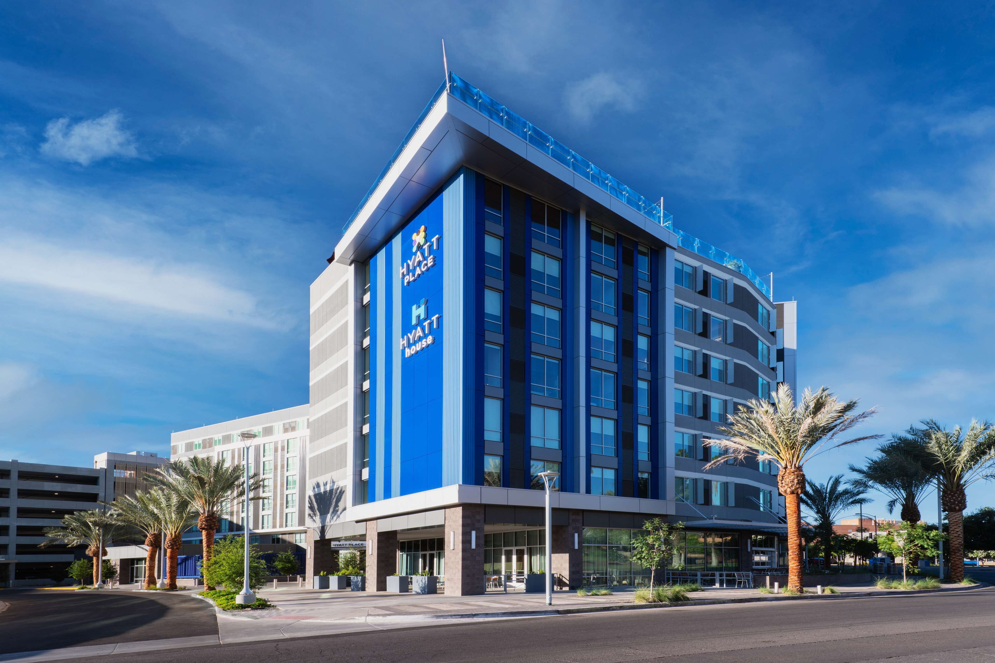 A modern Hyatt hotel with a prominent blue facade, multiple floors, and a parking garage in the background.