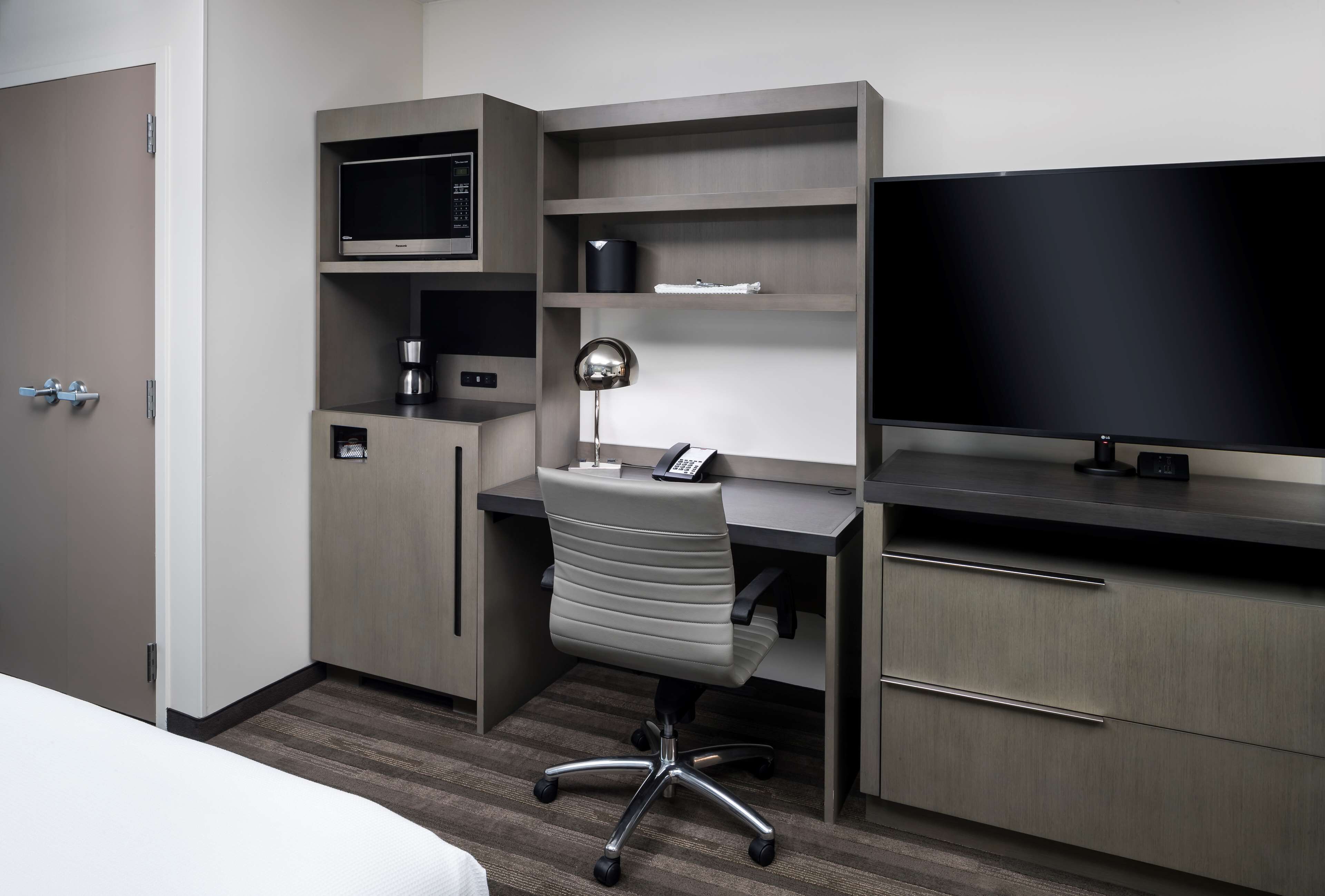 Une chambre d’hôtel équipée d’un lit, d’un bureau avec un ordinateur, d’un téléviseur à écran plat, d’une machine à café et d’une lampe.