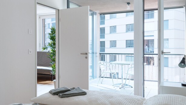 A modern bedroom with a large sliding glass door leading to a balcony. - Hitrental Messe Apartments (Basel)
