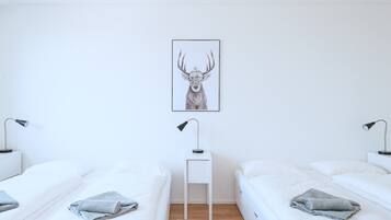 A minimalist bedroom with two beds, a small white table, and a framed deer artwork on the wall.