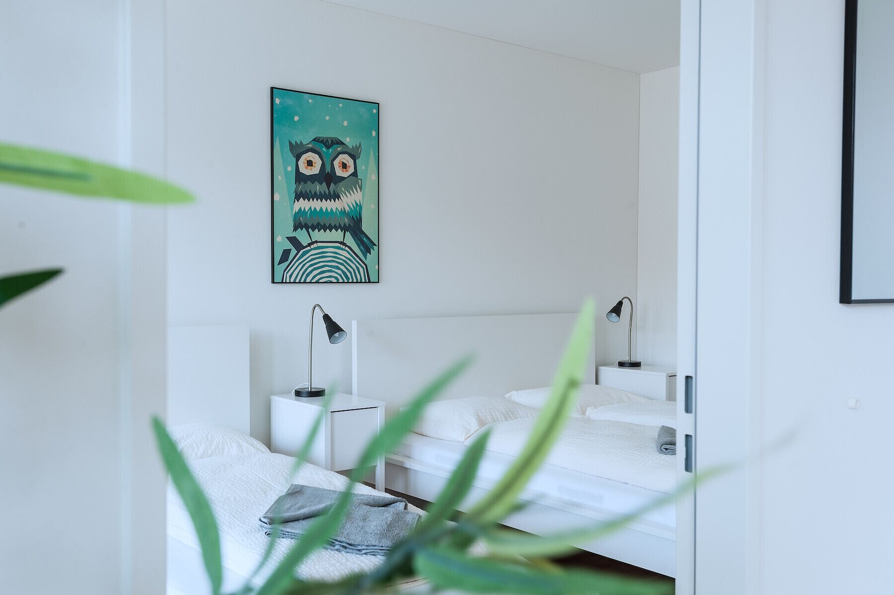 Une chambre avec deux lits, un tableau représentant une chouette accroché au mur et des lampes de chevet.