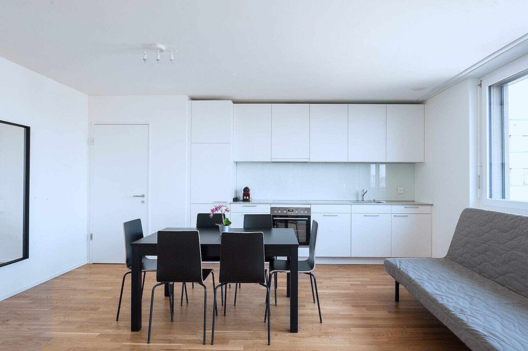 Un ambiente living moderno e minimalista con zona pranzo, cucina e un'ampia finestra che offre luce naturale.