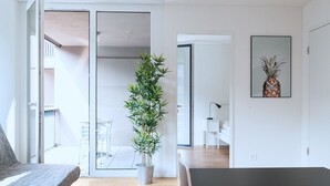 A modern, well-lit room with a wooden floor, a bed, a dining table with chairs, a potted plant, and a framed picture on the wall. - Hitrental Messe Apartments (Basel)
