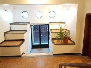 Enter through the glass door into a welcoming lobby with a potted plant and a comfortable bench.