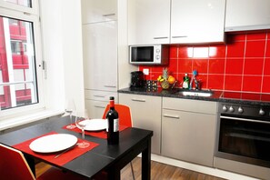 A kitchen with a microwave, a coffee maker, a bottle of wine, and a fruit bowl on the counter.