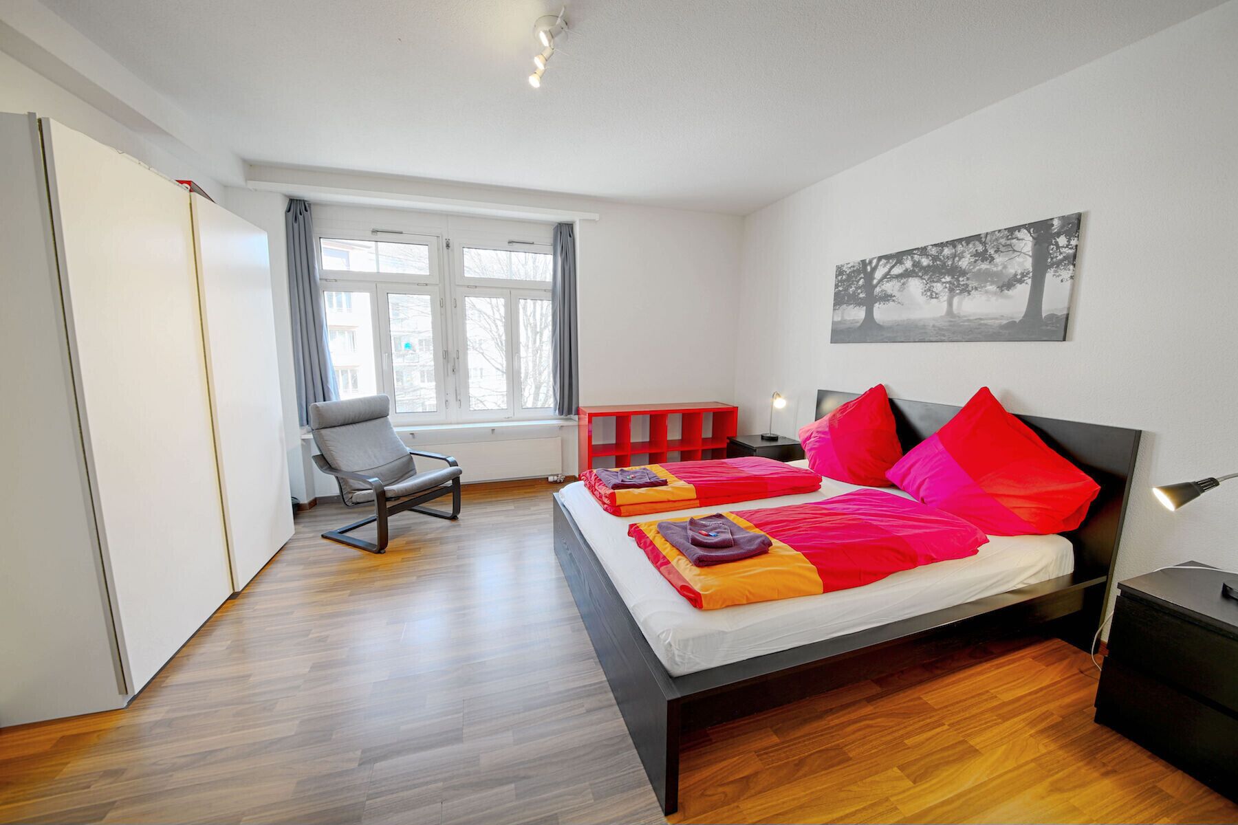 Un dormitorio moderno con cama, una silla, una ventana y una mesita de noche.