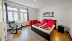 Quarto moderno com uma cama grande, uma cadeira, um móvel de armazenamento vermelho e um quadro na parede.