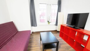 A room with a red sofa, a black table, and a red TV stand. - Hitrental Oerlikon Apartments (Zürich)