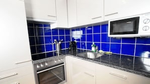 A kitchen with white cabinets, a black countertop, a stainless steel sink, a microwave, and a built-in oven. - Hitrental Oerlikon Apartments (Zürich)