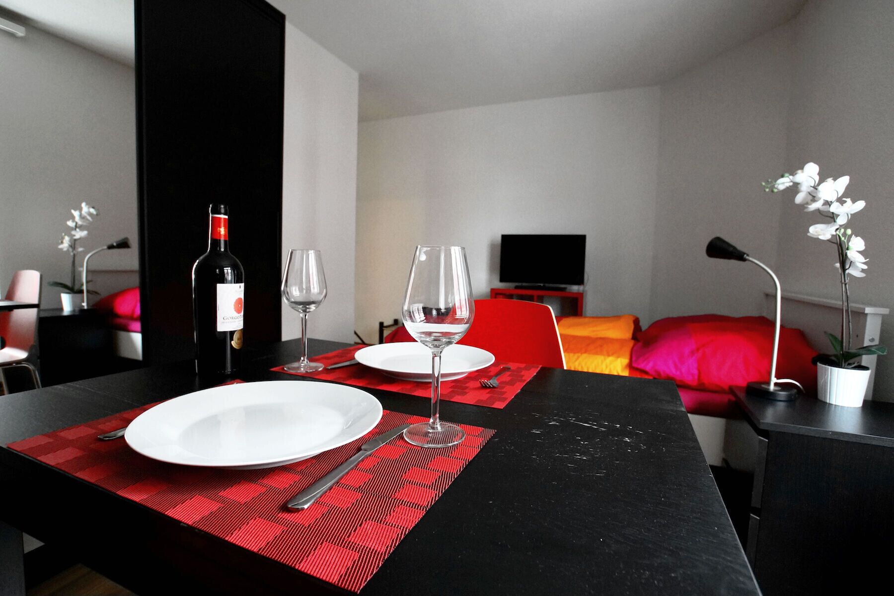 Un área de comedor con una mesa dispuesta para dos personas, una botella de vino y dos copas de vino.