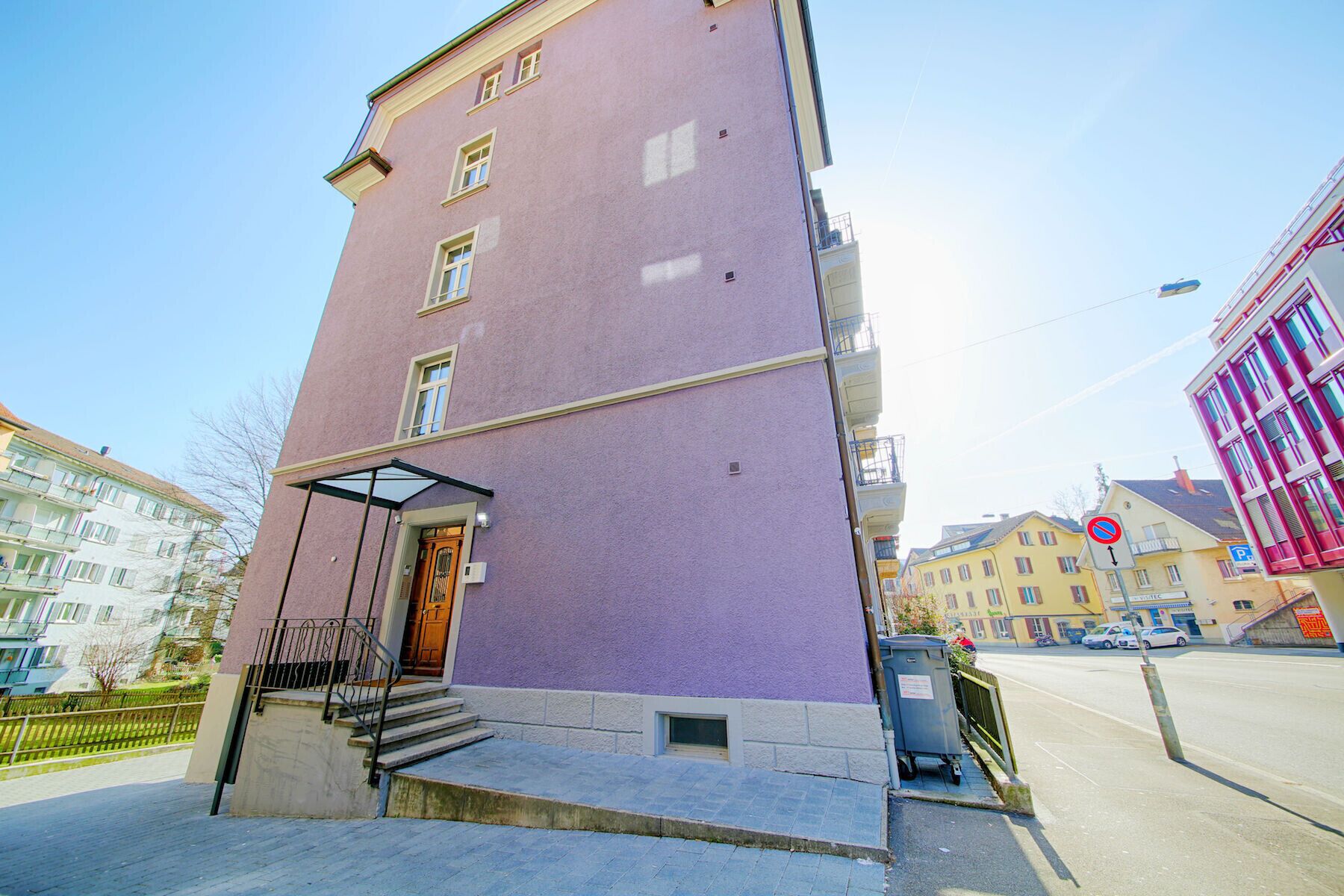 A multi-story building with a purple facade, a glass entrance, and a visible staircase leading to the entrance.