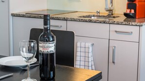 Une bouteille de vin et un verre sur une table dans une cuisine moderne, dotée de plans de travail en granit et d’appareils électroménagers en acier inoxydable.