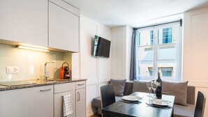 Une cuisine moderne avec un coin repas, un téléviseur à écran plat fixé au mur et une fenêtre avec des rideaux.
