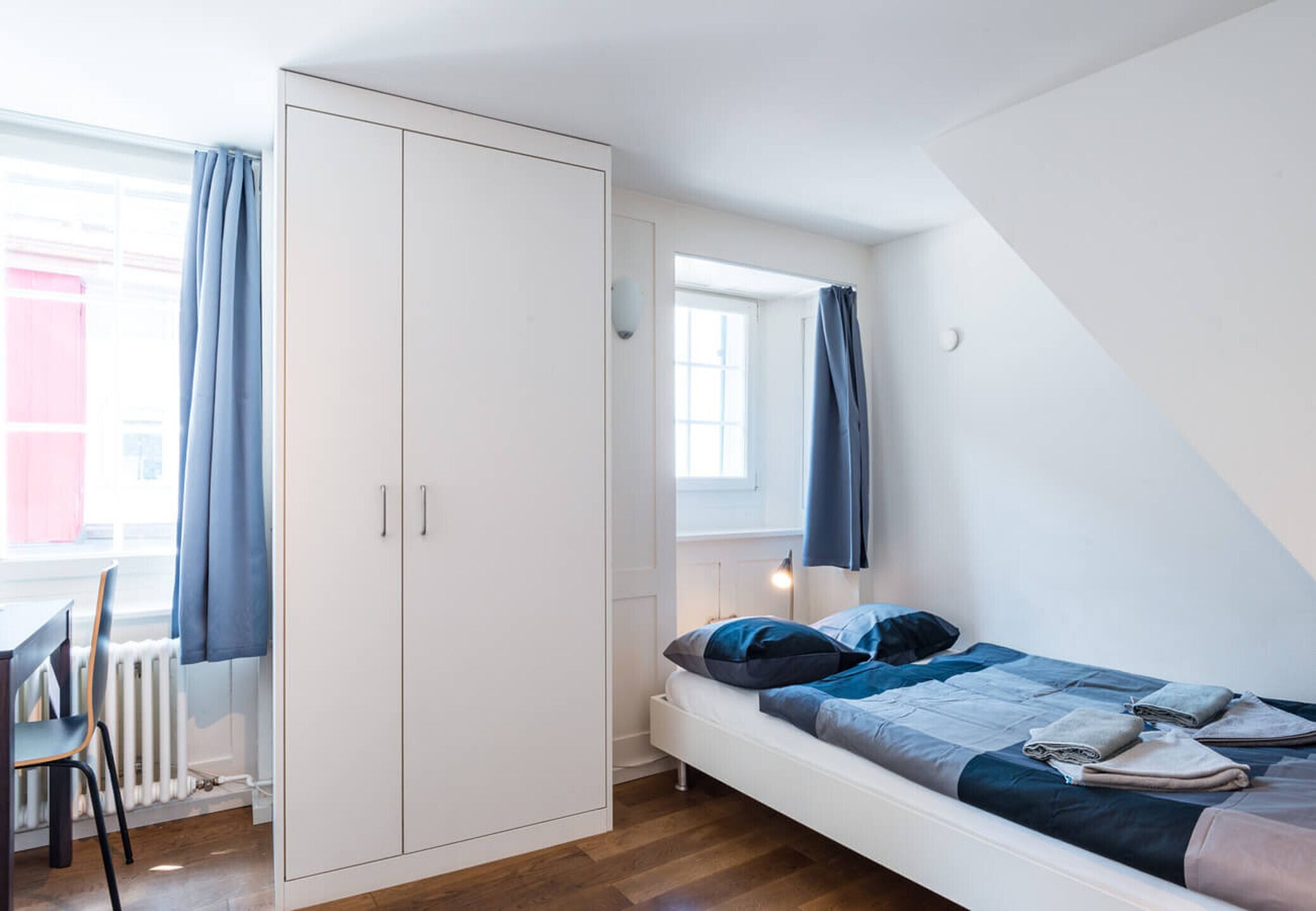 Een slaapkamer met een bed, een kledingkast, een raam met gordijnen en een radiator.