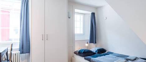 A bedroom with a bed, a wardrobe, a window with curtains, and a radiator.