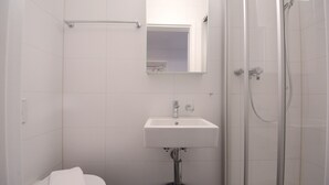 A bathroom with a white sink, a toilet, a glass shower enclosure, and a mirror above the sink. - Hitrental Station Apartments (Lucerne)