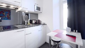 A compact kitchen with white cabinets, a microwave, a kettle, and a small table with a red mat. - Hitrental Station Apartments (Lucerne)