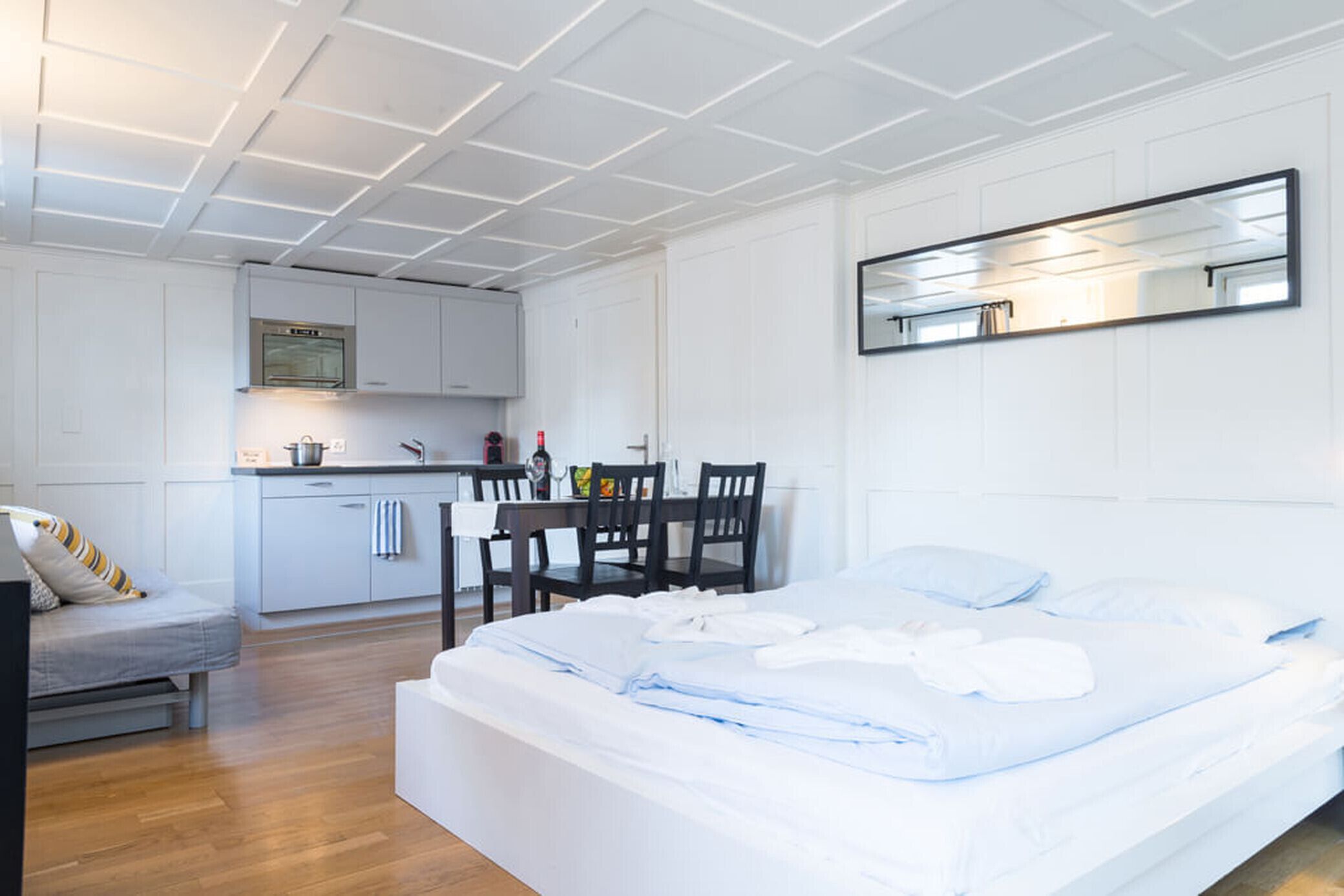 Une chambre moderne avec un grand lit, un coin repas comprenant une table et des chaises, et une kitchenette équipée de placards et d’une cuisinière.