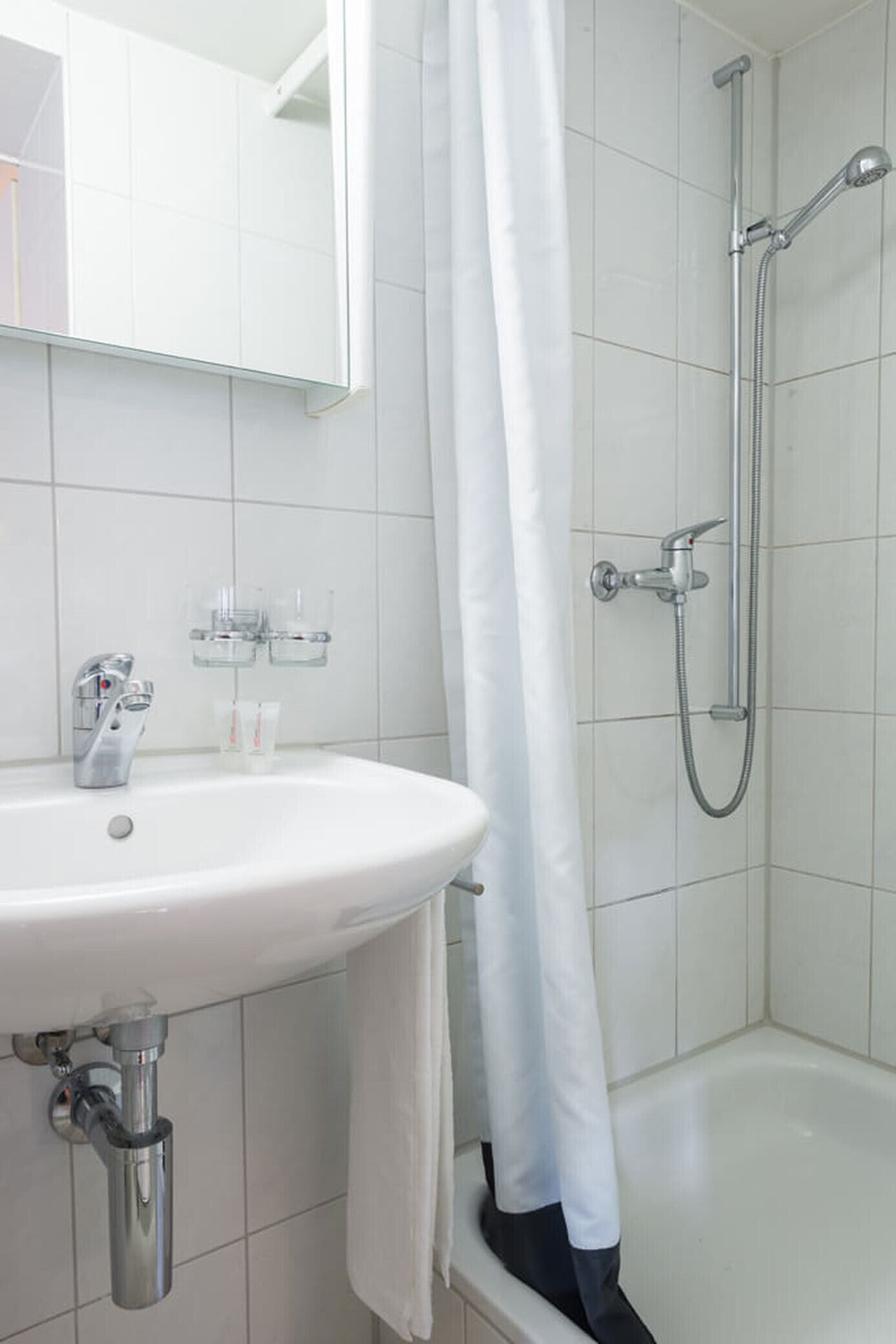 A bathroom with a white sink, a mirror, a shower with a handheld showerhead, and a bathtub.