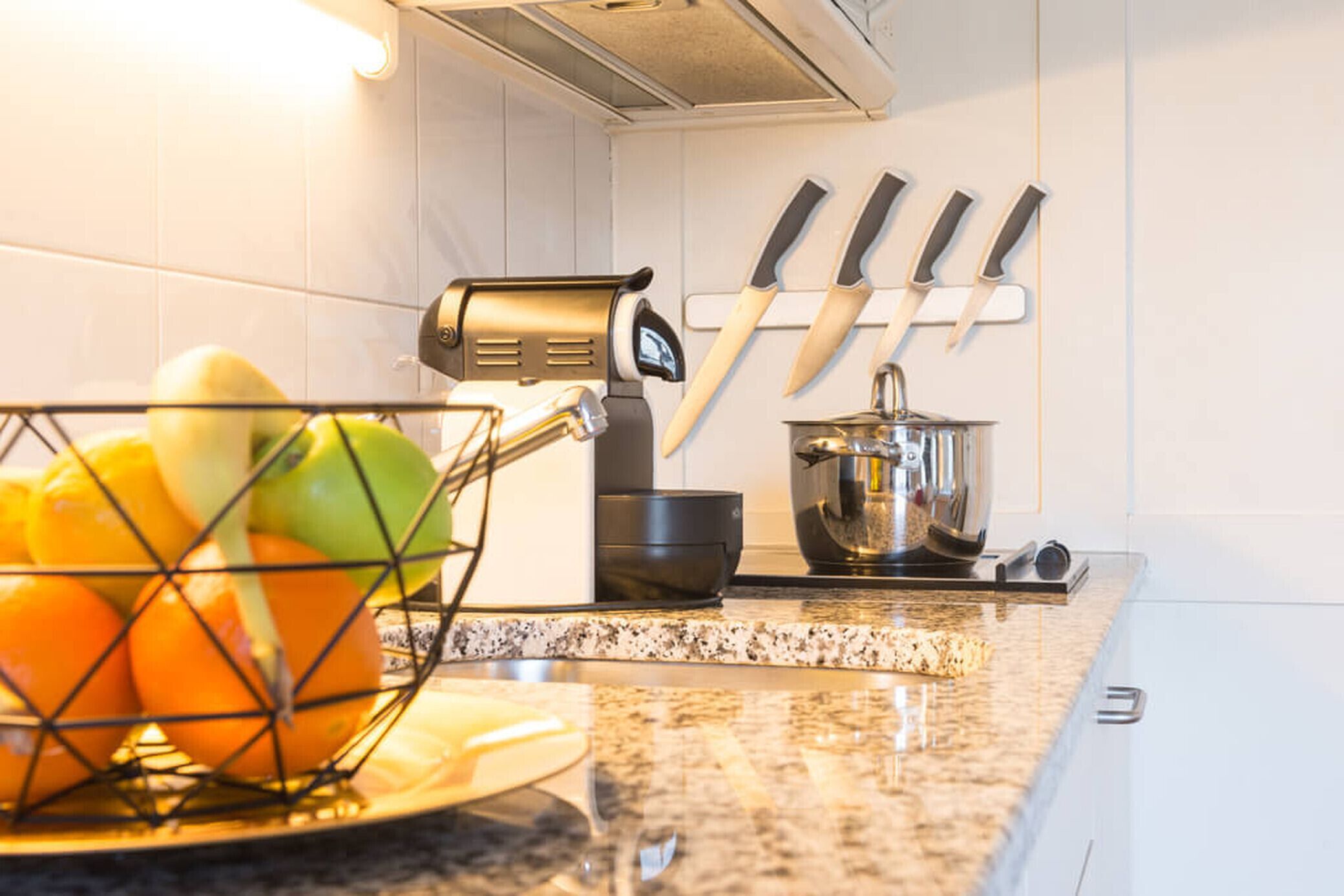 A kitchen with a fruit basket, a coffee machine, and knives on the wall.