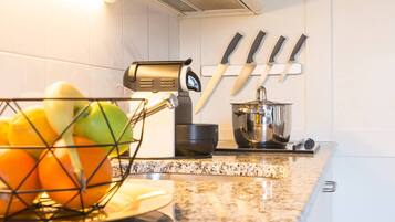 A kitchen with a fruit basket, a coffee machine, and knives on the wall.