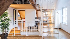 Un interior moderno con una escalera de madera y barandillas blancas, que conduce a una zona superior con vistas al exterior.