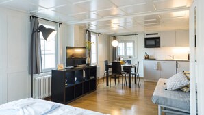 Una habitación de hotel moderna con cama, escritorio, televisor, zona de comedor y kitchenette.