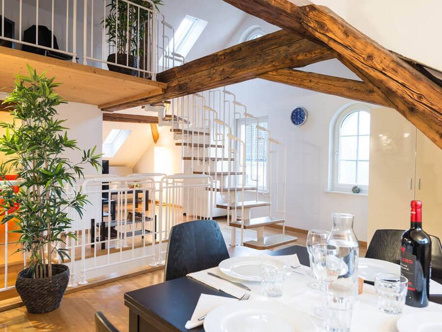 Un comedor con una mesa preparada para dos personas, una planta en maceta y una botella de vino.