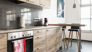 A modern kitchen with wooden cabinets, a stainless steel range hood, a coffee maker, and a dining area with two bar stools. - Exclusive vacation apartment in a unique location in the heart of Mittenwald. (Mittenwald)