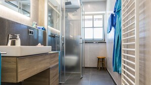 A modern bathroom with a glass shower enclosure, a sink with a wooden vanity, and a towel rack with blue towels. - Exclusive vacation apartment in a unique location in the heart of Mittenwald. (Mittenwald)