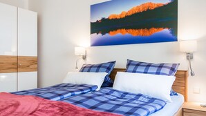 A bedroom with a bed, pillows, a blanket, a nightstand, a lamp, a wardrobe, and a painting of a mountain landscape. - Exclusive vacation apartment in a unique location in the heart of Mittenwald. (Mittenwald)