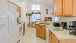 A kitchen with white appliances, wooden cabinets, a dining area with a table and chairs, and a window with a view. - Terra Verde Resort Home, Community Center 163 (Kissimmee)