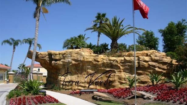 A rock formation with the name "Terra Verde" engraved on it, surrounded by a landscaped garden with red flowers and palm trees. - Terra Verde Resort Home, Community Center 163 (Kissimmee)