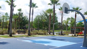 An outdoor basketball court with a blue surface, surrounded by palm trees and benches. - Terra Verde Resort Home, Community Center 163 (Kissimmee)