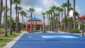 A basketball court with a blue surface, surrounded by palm trees and a playground with a red slide. - Terra Verde Resort Home, Community Center 163 (Kissimmee)