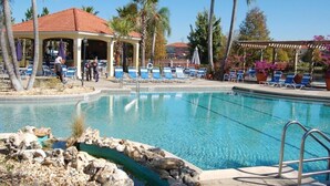 A clear blue pool with lounge chairs and a covered seating area, surrounded by palm trees. - Terra Verde Resort Home, Community Center 163 (Kissimmee)