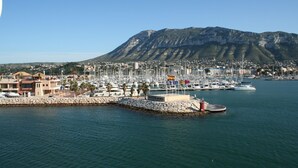 Una marina con barche, un muro in pietra e una montagna sullo sfondo.