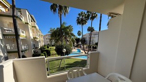 Un balcone con vista su una piscina, palme e edifici circostanti.
