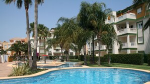 Una piscina circondata da palme e un edificio a più piani con balconi.