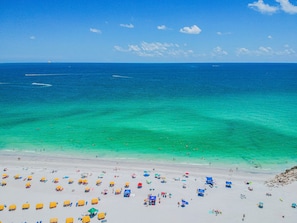 A beach with clear turquoise waters, a sandy shore, and numerous umbrellas and beach chairs.