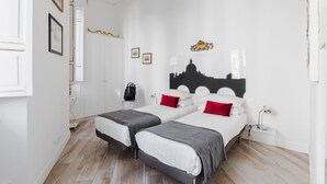 A room with two beds, a nightstand, a desk, and a wall-mounted picture.