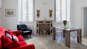 A living room with a red sofa, black armchair, fireplace, and a dining table with clear chairs.