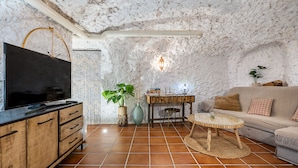 A cozy living room with a television, wooden cabinet, tiled floor, and a stone wall. - Cueva del rey chico, Sacromonte. (Granada)