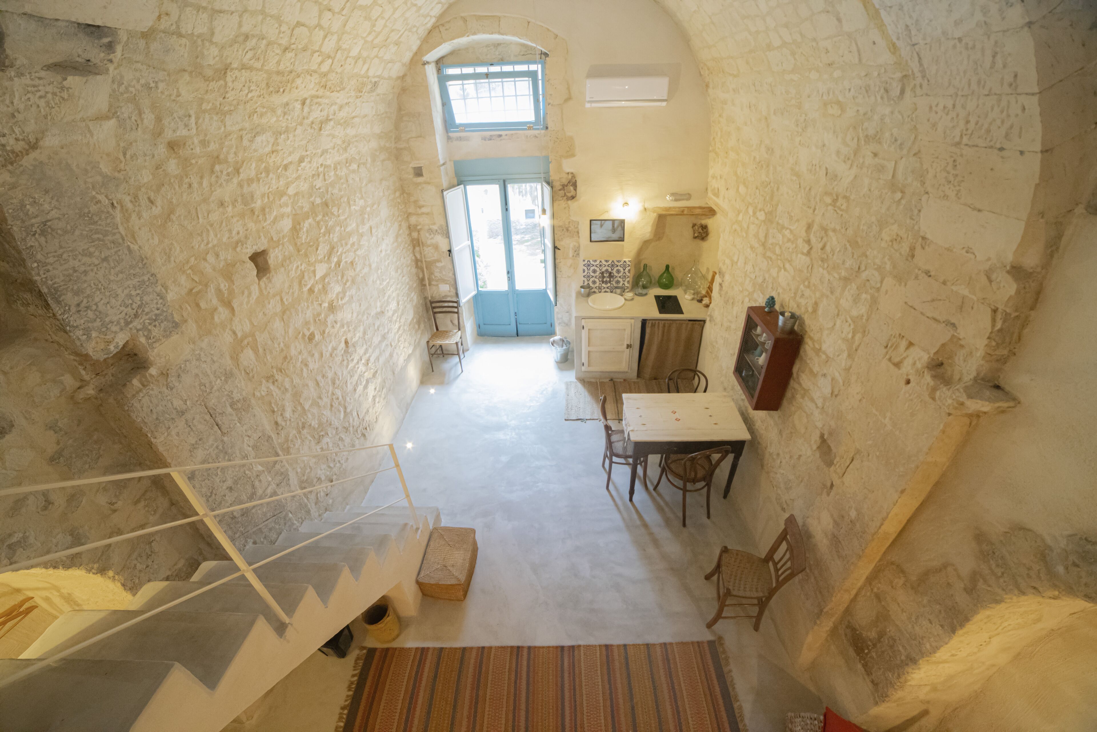 Ein Zimmer mit Steinwänden, einer Wendeltreppe, einer Essecke mit Tisch und Stühlen sowie einer Küchenzeile mit Spüle und Arbeitsfläche.